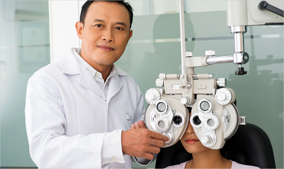 Médico oftalmólogo sonriendo mientras le realiza una prueba a una paciente.