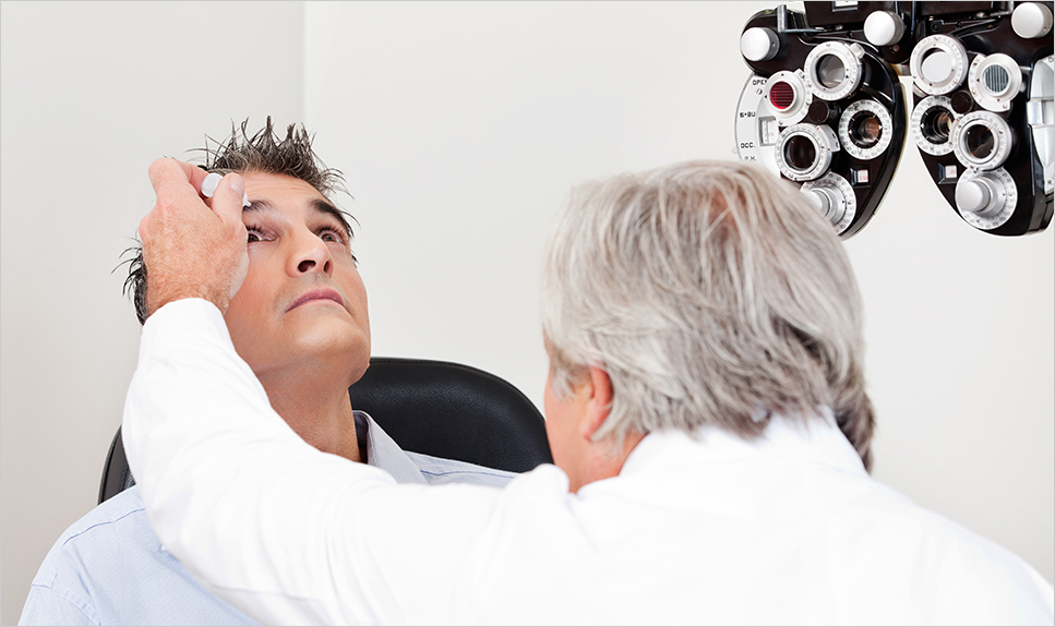Médico oftalmóogo aplicando gotas en los ojos de un paciente.