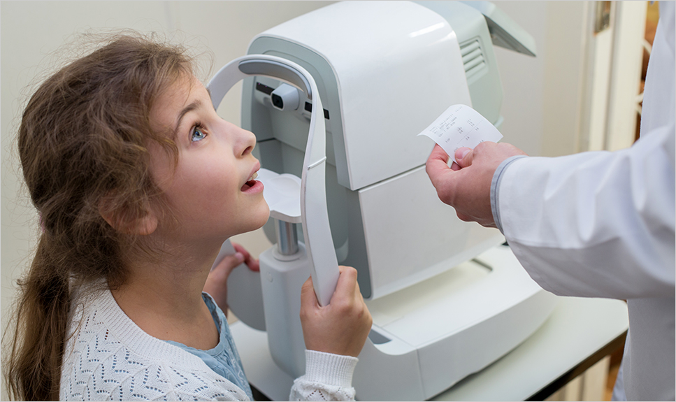 Niña con aparato oftalmológico viendo al médico.